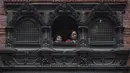 Orang-orang menonton dari jendela saat umat mengambil bagian dalam prosesi saat para imam membawa Seto Machindranath, dewa pelindung Nepal, selama festival kereta di Kathmandu (9/4/2022). (AFP/Prakash Mathema)