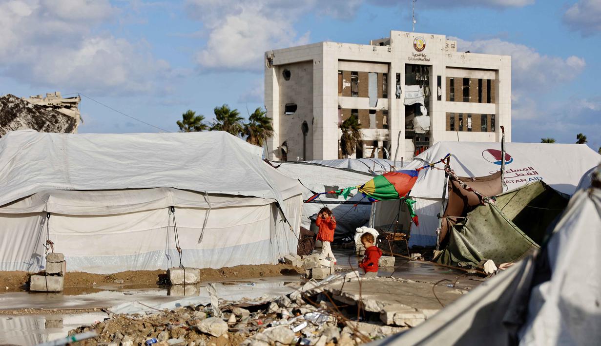 Diketahui, kondisi cuaca saat ini telah menjadi ancaman nyata bagi warga Palestina yang terpaksa tinggal di tenda-tenda usang atau bangunan yang sangat berisiko roboh. Tampak dalam foto, anak-anak pengungsi Palestina bermain di luar tenda tempat tinggal mereka saat Mediterania timur mengalami musim dingin yang dingin dan basah, di Kota Gaza pada 28 Desember 2025. (Omar AL-QATTAA/AFP)