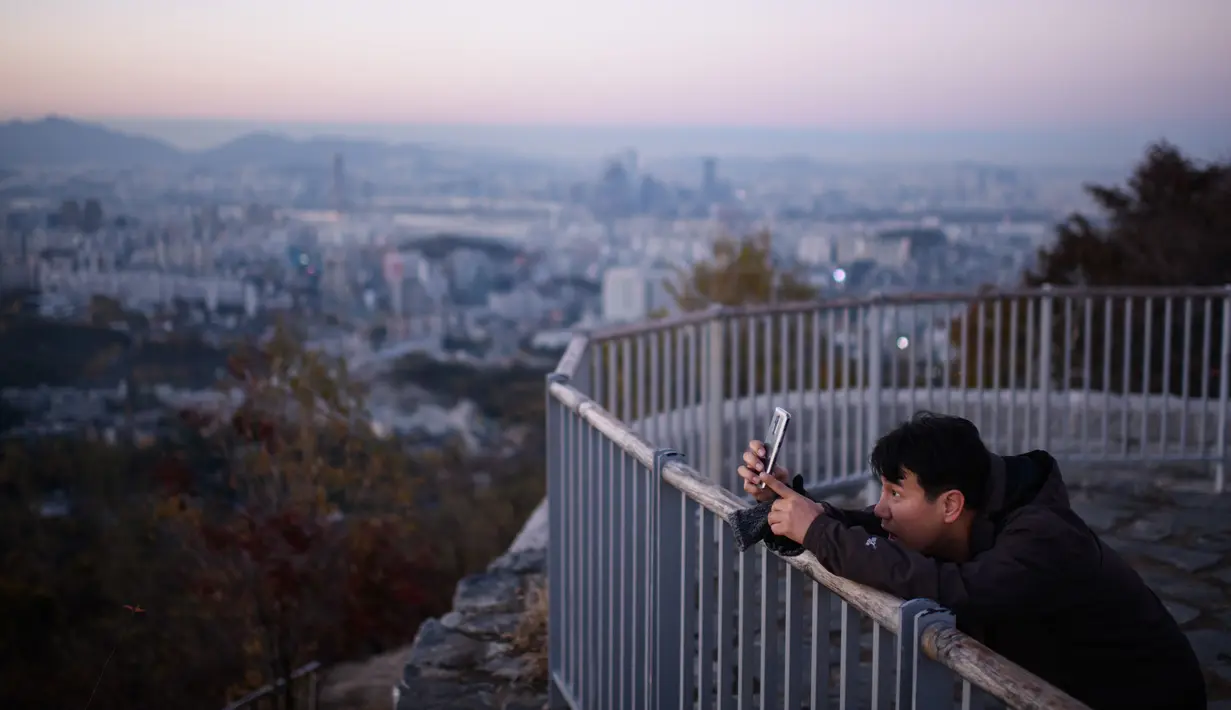 Seorang pejalan kaki mengabadikan kota Seoul selama matahari terbit di Korea Selatan (31/10). Kota Seoul juga merupakan pusat bisnis, keuangan, perusahaan multinasional, dan organisasi global. (AFP Photo/Ed Jones)