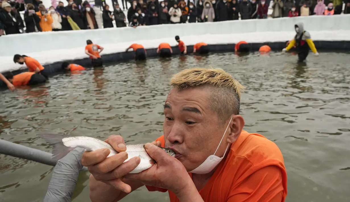 Seorang peserta memegang trout di mulut setelah menangkapnya selama kontes menangkap ikan di Hwacheon, Korea Selatan, Sabtu (7/1/2023). Kontes ini merupakan bagian dari festival es tahunan yang menarik lebih dari satu juta pengunjung setiap tahun. (AP Photo/Ahn Young-joon)
