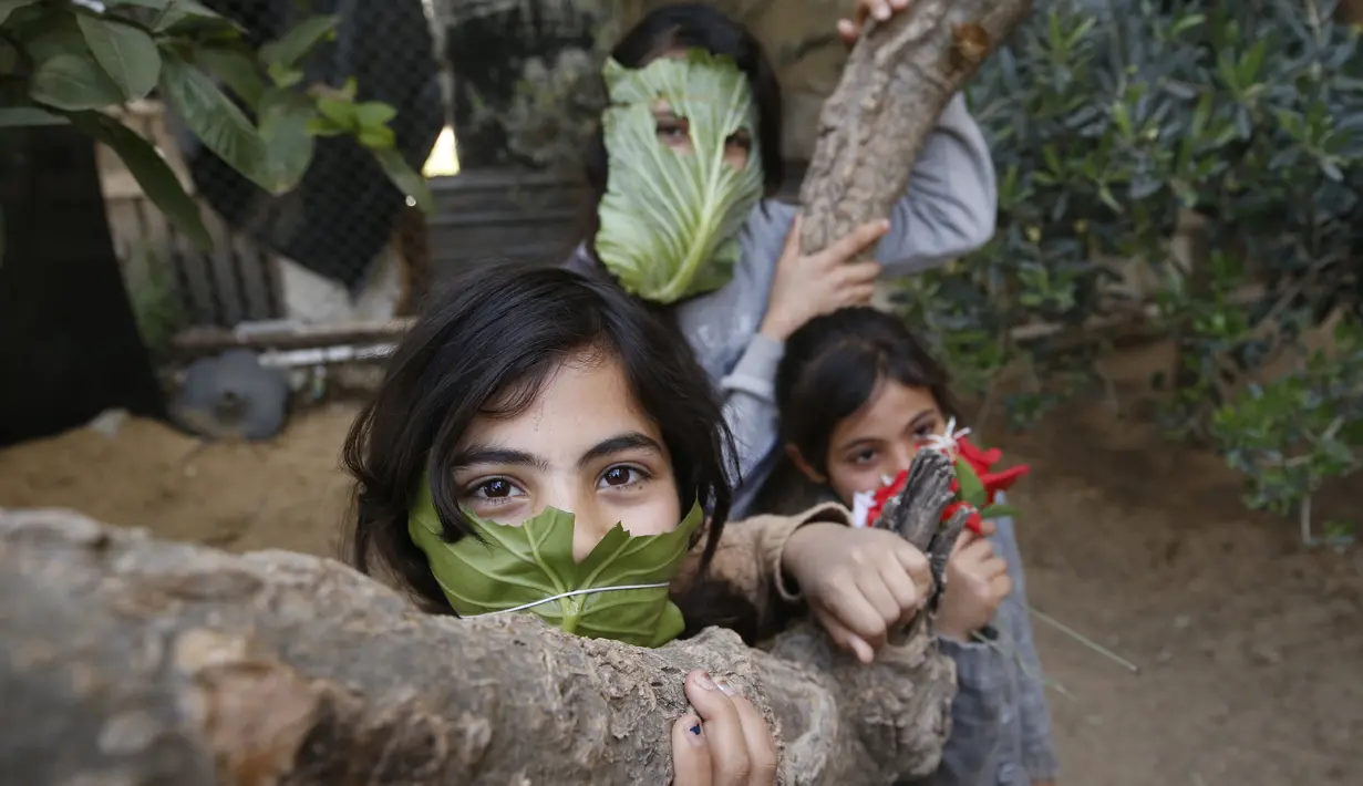 Tiga anak Palestina berpose dengan masker yang terbuat dari kubis di halaman rumahnya di Beit Lahia di Jalur Gaza utara (16/4/2020).  (AFP/Mohamed Abed)