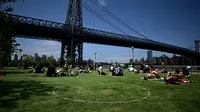 Orang-orang berusaha menjaga jarak dalam lingkaran putih saat bersantai di Domino Park, Brooklyn di Kota New York, Minggu (17/5/2020). Pengunjung taman berjemur dengan tetap menerapkan protokol penularan coorna Covid-19. (Photo by Johannes EISELE / AFP)
