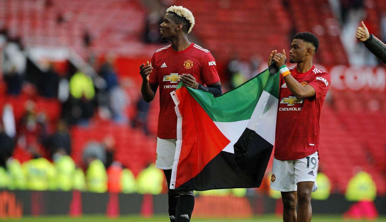 Tak lama berselang, Amad Diallo mengikuti Pogba untuk bersama-sama membentangkan bendera tersebut dan menunjukkannya ke arah penonton di tribun Old Trafford. (Foto: AFP/Pool/Phil Noble)