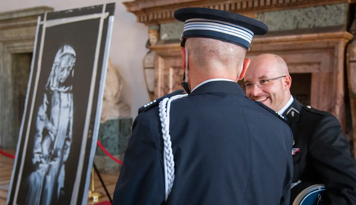 Petugas Gendarmerie Prancis melihat lukisan seniman Inggris Banksy yang menggambarkan sosok perempuan muda dengan ekspresi sedih di ruang musik Bataclan di Paris, selama upacara di Kedutaan Besar Perancis di Roma (14/7/2020). (AP/Photo/Domenico Stinellis)