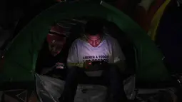Sebagian keluarga tahanan memilih berkemah di luar penjara El Rodeo I di Guatire, Negara Bagian Miranda, sekitar 30 kilometer sebelah timur Caracas, Venezuela. Tampak dalam foto, seorang pria menggunakan telepon seluler di atas tenda yang didirikan oleh kerabat tahanan politik di luar penjara El Rodeo I di Guatire, Negara Bagian Miranda, sekitar 30 kilometer sebelah timur Caracas, Venezuela, pada 12 Januari 2026. (Pedro MATTEY/AFP)