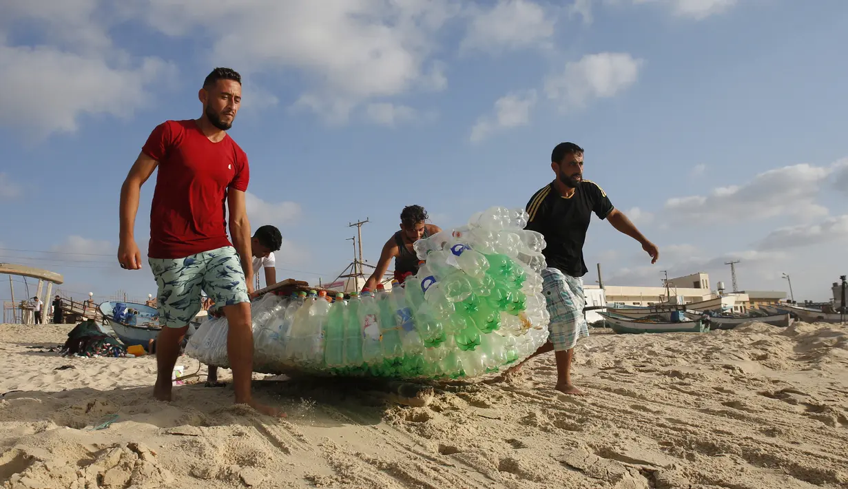 Nelayan Palestina, Mouad Abu Zeid (kanan) dan teman-temannya membawa perahu yang terbuat dari botol plastik bekas di sebuah pantai di Rafah, Jalur Gaza, 14 Agustus 2018. Zeid menggunakan 700 botol plastik bekas menjadi sebuah perahu. (AFP/SAID KHATIB)