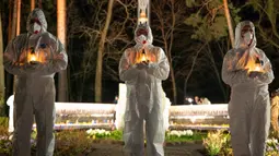Orang-orang yang mengenakan pakaian pelindung putih memegang lilin selama upacara peringatan yang didedikasikan untuk petugas pemadam kebakaran dan pekerja yang meninggal setelah bencana nuklir Chernobyl, menjelang peringatan 40 tahunnya di Slavutych, Ukraina, Sabtu, 25 April 2026. (AP Photo/Dan Bashakov)