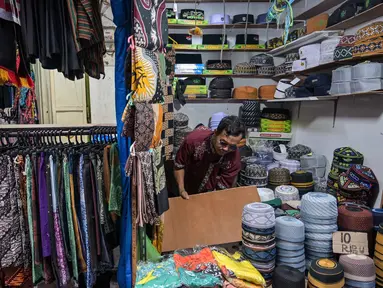 Seorang pedagang menata peci untuk dijual selama bulan suci Ramadan di dekat Masjid Sunan Ampel, Surabaya, Jawa Timur, pada Minggu 8 Maret 2026. Sepanjang Ramadan, kawasan sekitar Masjid Sunan Ampel, Surabaya, Jawa Timur, berubah menjadi pusat belanja dan kuliner yang kental dengan nuansa Timur Tengah. (JUNI KRISWANTO/AFP)
