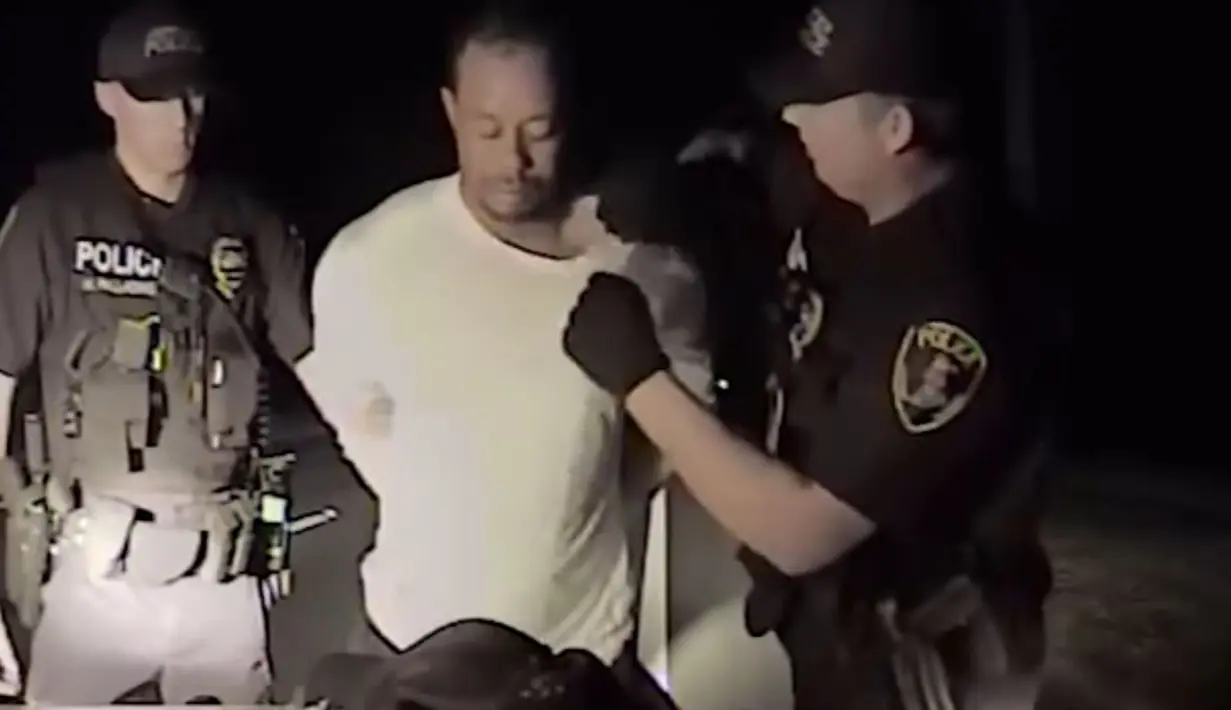 Dalam gambar yang diambil dari video terlihat pegolf ternama AS, Tiger Woods ditangkap dua polisi di Jupiter, Florida, 29 Mei 2017. Tiger Woods harus berurusan dengan pihak kepolisian karena menyetir dalam keadaan mabuk (HO/ Jupiter Police Department/AFP)