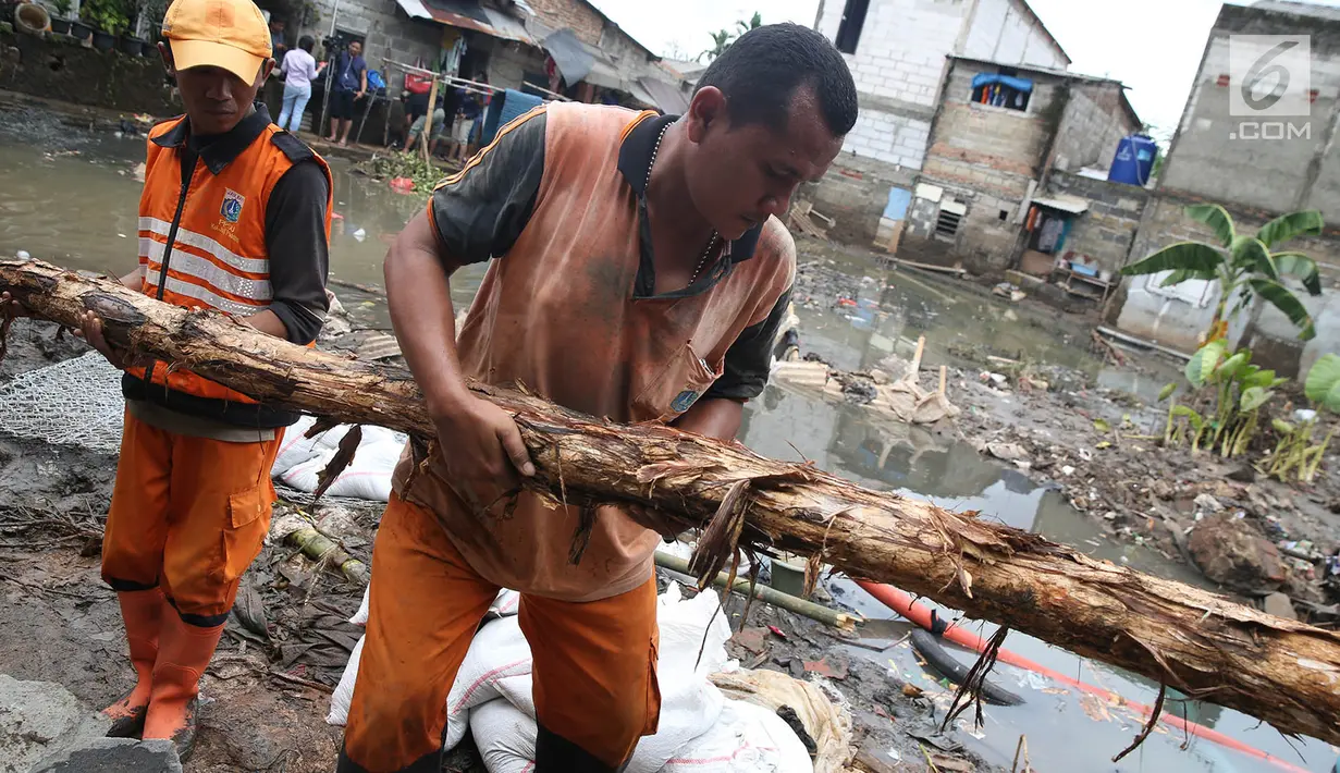 Pasukan oranye membawa kayu untuk memperbaiki tanggul yang jebol di kawasan Jatipadang, Jakarta Selatan, Selasa (12/12). Perbaikan tanggul sementara itu dilakukan dengan membuat tanggul pasir lalu menahannya dengan kayu. (Liputan6.com/Immanuel Antonius)