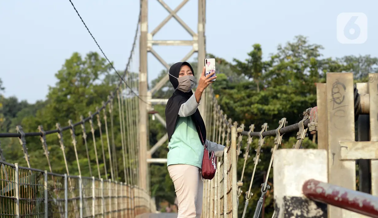 Warga asyik berswafoto di atas jembatan gantung, Kelurahan Curug, Bojongsari, Kota Depok, Jawa Barat, Senin (24/8/2020). Setiap sore, warga sekitar bermain di jembatan tersebut sambil menikmati matahari tenggelam. (merdeka.com/Dwi Narwoko)