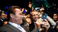 Aktor yang juga mantan Gubernur California, Arnold Schwarzenegger berswafoto bersama Presiden Prancis, Emmanuel Macron dan wisatawan dengan latar belakang Menara Eiffel seusai KTT One Planet Summit di Paris, Selasa (12/12). (AP/Thibault Camus, Pool)