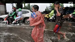Anak-anak penjual jas hujan dan ojek payung bermain air saat banjir menggenangi Jalan DI Panjaitan, Jakarta, Senin (3/12).  Menurut petugas, banjir disebabkan oleh buruknya sistem drainase atau gorong-gorong. (Merdeka.com/ Iqbal S. Nugroho)