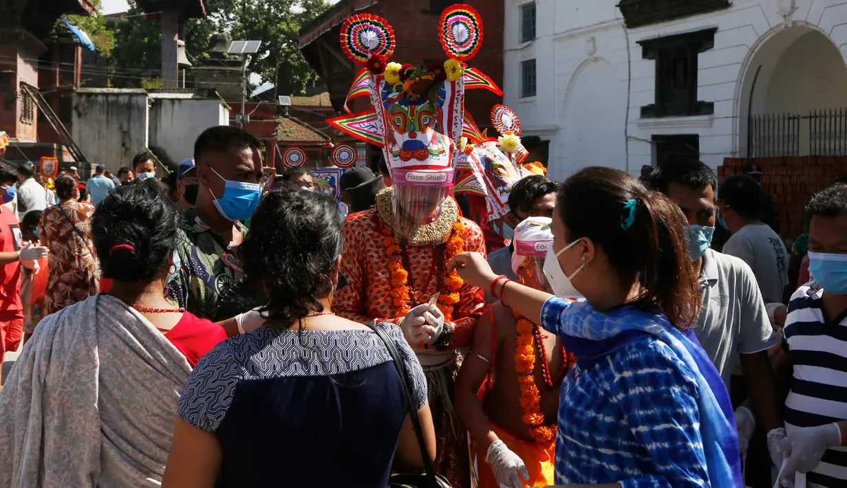 Anggota komunitas Newar mengenakan kostum dan masker saat berpartisipasi dalam prosesi 'Gai Jatra', atau festival sapi, di Kathmandu, Nepal, Selasa (4/8/2020). Festival ini untuk meminta keselamatan dan kedamaian bagi orang yang mereka cintai yang telah meninggal. (AP Photo/Niranjan Shrestha)