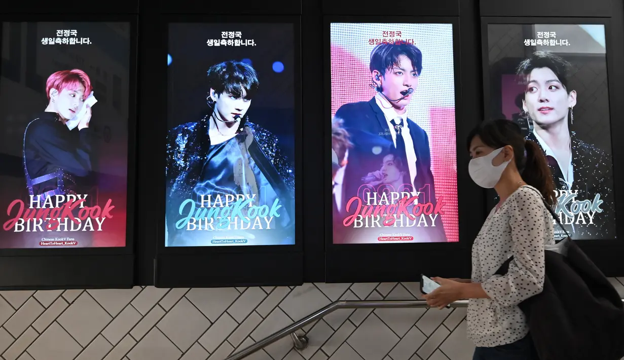 Seorang perempuan melewati layar listrik yang menunjukkan anggota boyband K-pop, BTS, di di stasiun kereta bawah tanah di Seoul, Selasa (1/9/2020). Bangtan Boys (BTS) menjadi artis Korea Selatan pertama yang berhasil menempati puncak Billboard Hot 100 dengan lagu Dynamite. (Jung Yeon-je/AFP)