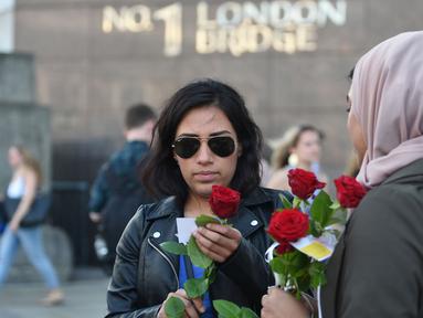 Mawar yang disertai sebuah pesan dibagikan kepada para pejalan kaki di London Bridge, Minggu (11/6). Muslim Inggris membagikan ratusan mawar sebagai bentuk solidaritas menyusul serangan teror London yang terjadi pekan lalu. (David Mirzoeff/PA via AP)