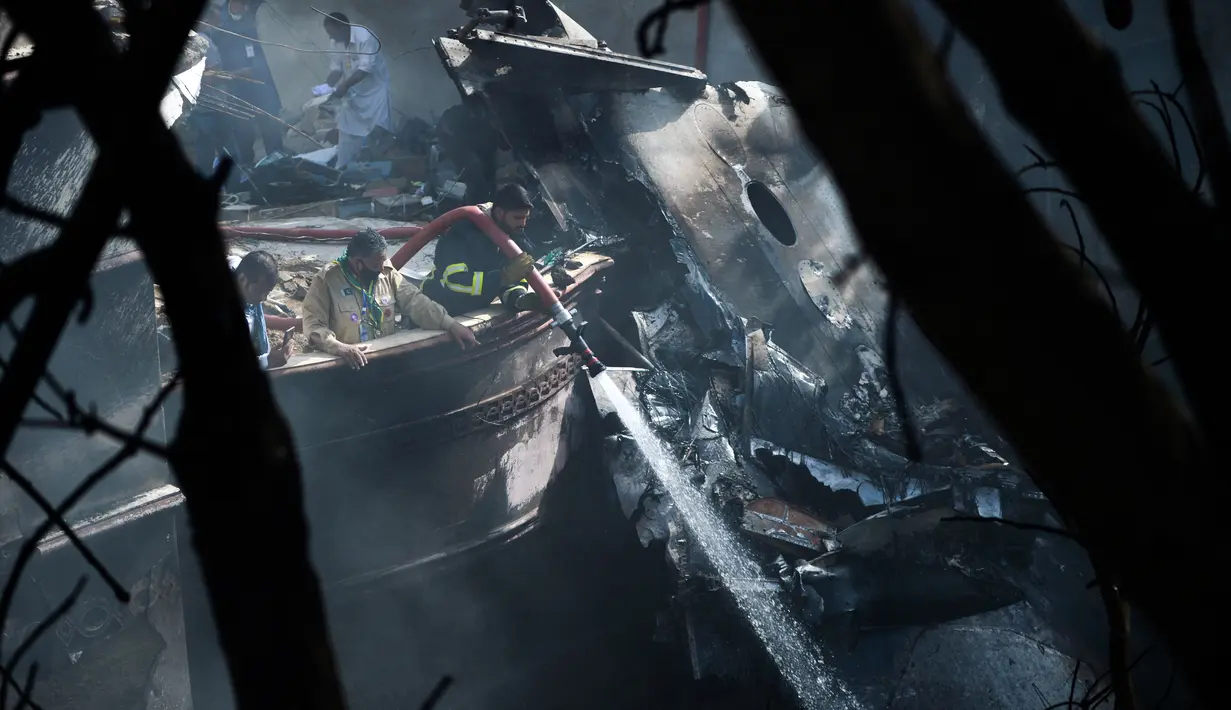 Petugas pemadam kebakaran menyemprotkan air pada puing pesawat Pakistan International Airlines yang jatuh di Karachi, Pakistan, Jumat (22/5/2020). Pesawat nahas dengan nomor penerbangan PK8303 mengangkut 91 penumpang dan delapan awak pesawat. (Rizwan TABASSUM/AFP)