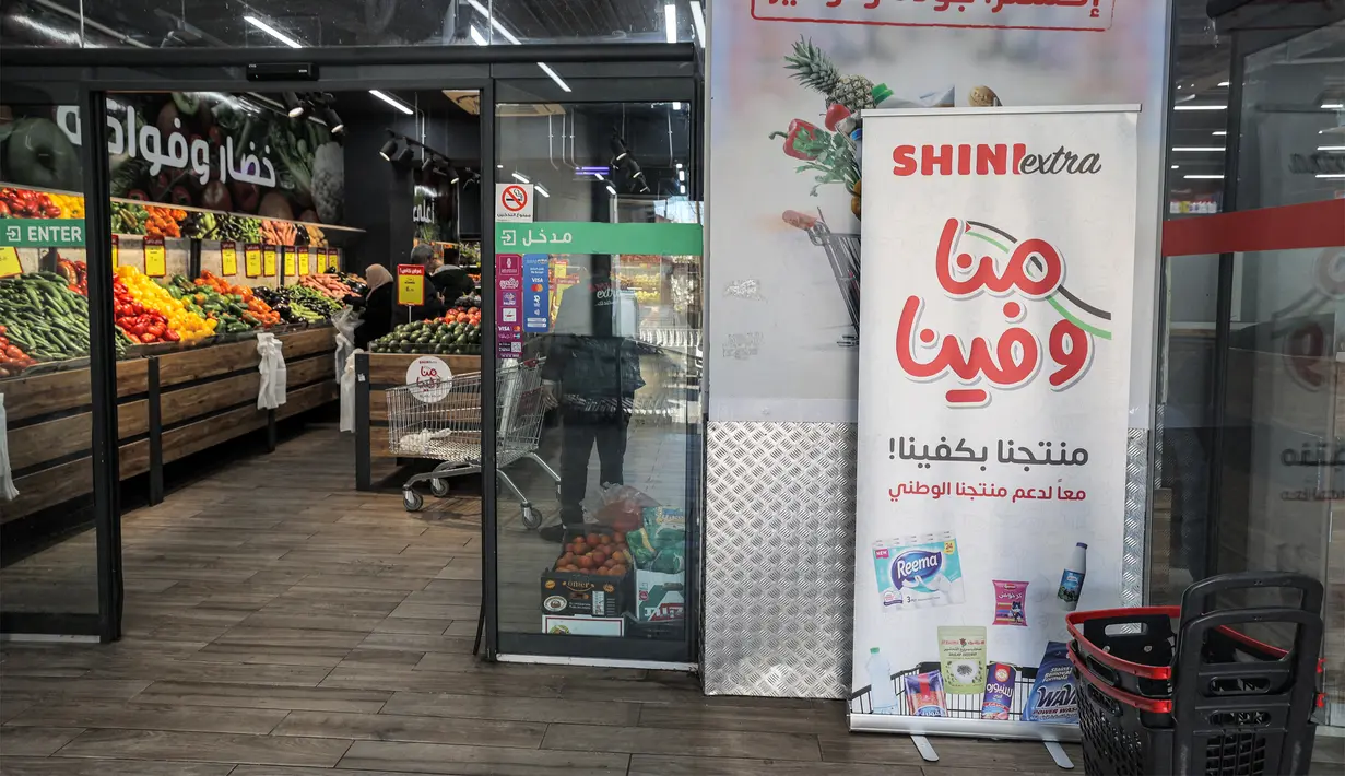 Spanduk yang mengidentifikasi produk lokal dipajang di pintu masuk sebuah supermarket di Ramallah di Tepi Barat yang diduduki, sebagai bagian dari kampanye yang lebih luas yang mendesak warga Palestina untuk memboikot produk Israel dan membeli barang-barang buatan lokal, Selasa (26/12/2023). (Jaafar ASHTIYEH / AFP)