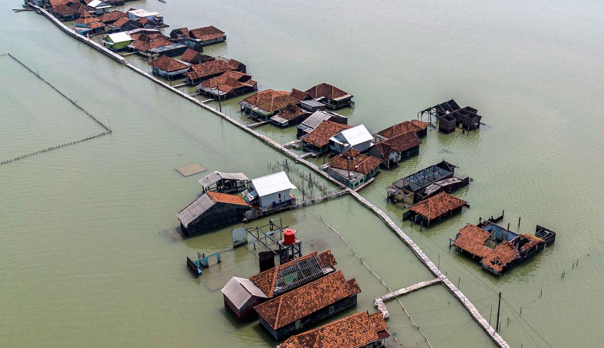 Penurunan tanah (land subsidence), kenaikan muka air laut akibat perubahan iklim, dan kurang maksimalnya mitigasi/infrastruktur pertahanan pesisir menjadi beberapa penyebab semakin tenggelamnya Desa Timbulsloko di Sayung, Demak, Jawa Tengah. Tampak dalam foto, pemandangan udara menunjukkan rumah-rumah nan sebagian terendam air laut akibat banjir pasang surut di sepanjang pantai selatan Laut Jawa di desa Timbulsloko, Demak, Jawa Tengah pada Sabtu 18 April 2026. (DEVI RAHMAN/AFP)