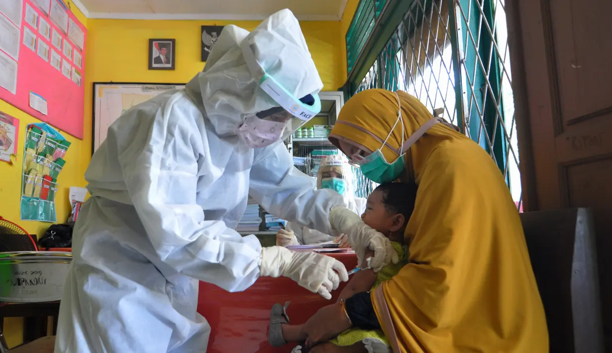 Perawat mengenakan alat pelindung diri saat menyuntikkan vaksin campak kepada seorang anak di Hari Perawat Internasional di Palu, Indonesia, Selasa (12/5/2020). Hari Perawat Internasional diperingati setiap tanggal 12 Mei yang bertepatan dengan kelahiran Florence Nightingale. (MUHAMMAD RIFKI/AFP)