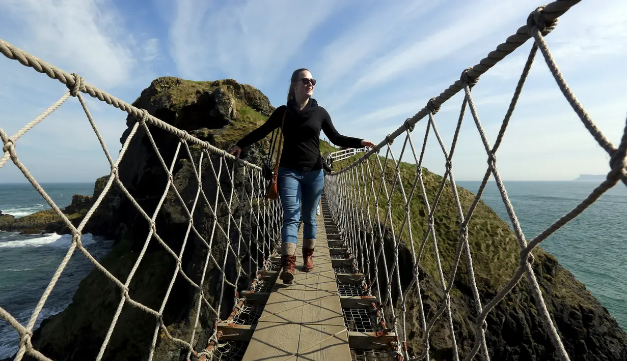 Seorang turis wanita berdiri ditengah Jembatan Carrick-a-Rede Rope di Pantai Causeway, Irlandia Utara, Rabu (8/4/2015). Jembatan unik ini memiliki panjang 19 meter dan berada di ketinggian 30 meter di atas karang laut. (REUTERS/Cathal McNaughton)