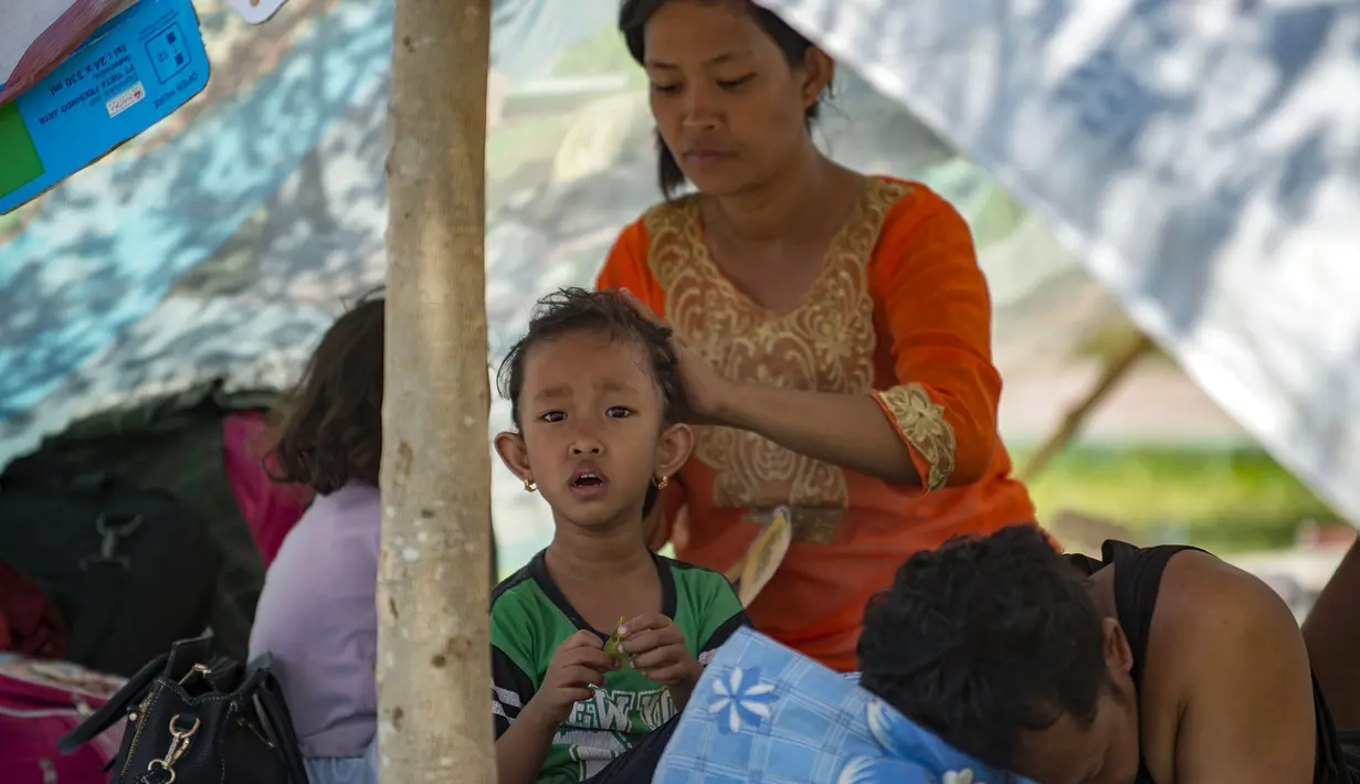 Seorang ibu dan anaknya berteduh di sebuah taman setelah gempa dan tsunami melanda Palu di Sulawesi Tengah, Selasa (2/10). Data terbaru BNPB menunjukkan, korban tewas akibat tsunami dan gempa di Sulawesi Tengah sudah mencapai 1.347 orang. (AFP/BAY ISMOYO)