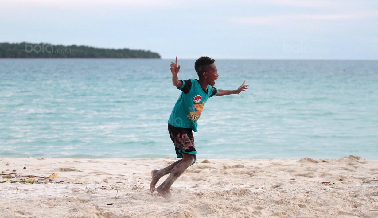 Seorang bocah melakukan selebrasi usai mencetak gol saat bermain bola dekat pantai di Desa Matwaer, Kei Kecil, Maluku (25/12/2017). Bermain bola di pasir menjadi daya tarik tersendiri bagi anak-anak dan pemuda desa. (Bola.com/Nick Hanoatubun)