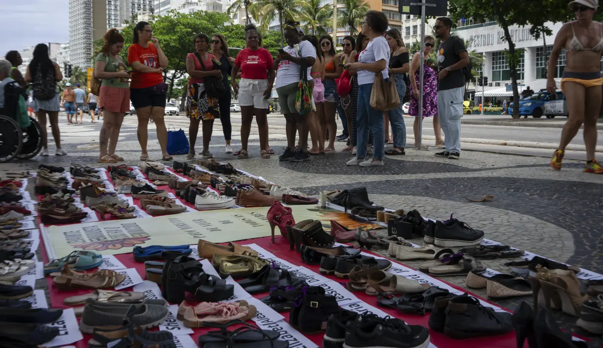 Orang-orang melihat sepatu dengan nama-nama perempuan korban femisida di Brasil dalam acara Hari Internasional untuk Penghapusan Kekerasan terhadap Perempuan di Pantai Copacabana, Rio de Janeiro, Sabtu (25/11/2023). (Tercio TEIXEIRA / AFP)
