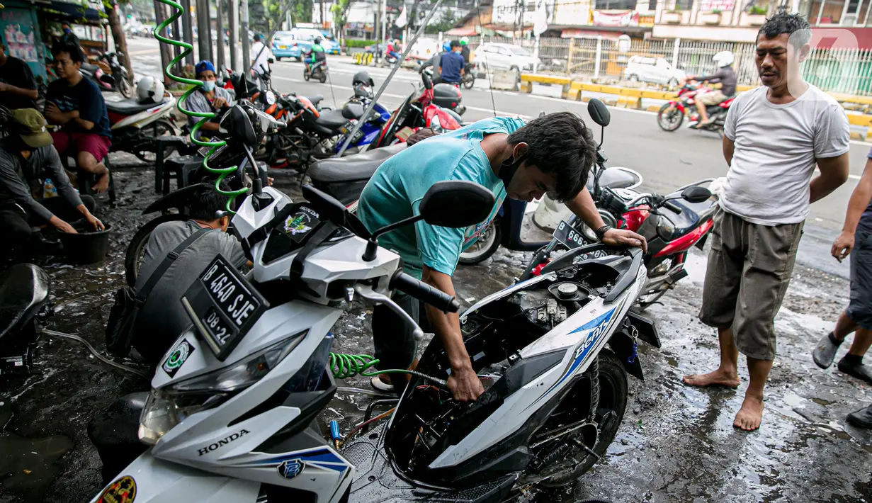 Montir membersihkan sepeda motor konsumen usai terendam banjir di kawasan Mampang, Jakarta, Minggu (21/2/2021). Banjir yang melanda Ibu Kota Jakarta pada Sabtu (20/2) menyebabkan banyak kendaraan warga mengalami kerusakan akibat terendam air. (Liputan6.com/Faizal Fanani)