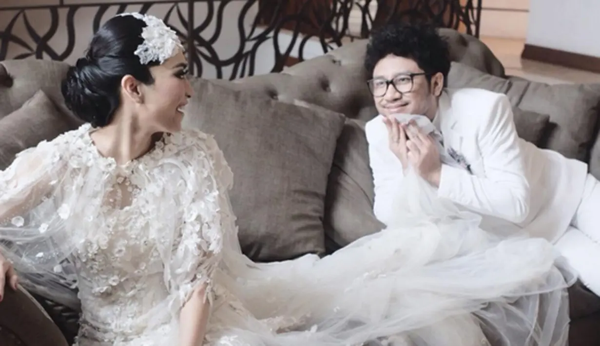 Nampak Kunto Aji dan istri duduk di sebuah sofa dan memakai busana pengantin modern bernuansa putih. Sisi humoris Kunto Aji terlihat disini, ia justru menarik gaun sang istri dan menutupi sebagian wajahnya. (via instagram/@uchiet)