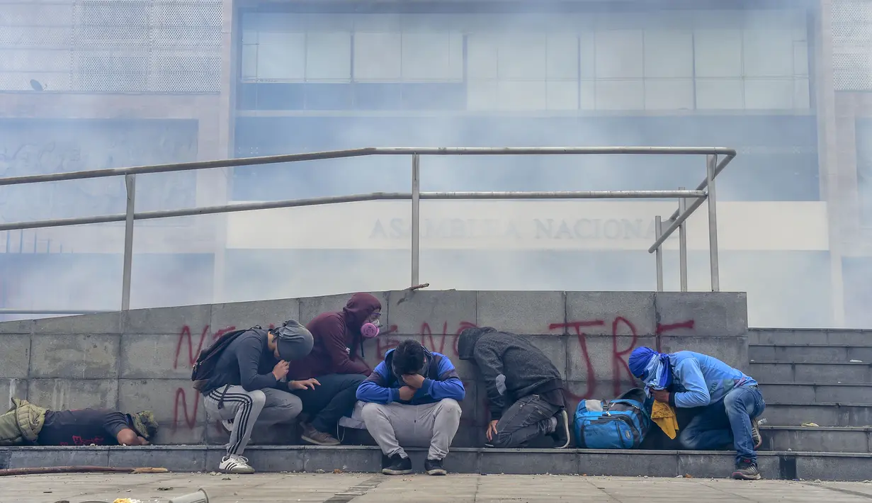 Demonstran berlindung setelah polisi anti huru hara menembakkan gas air mata untuk membubarkan kerumunan pengunjuk rasa dari gedung parlemen di Quito (8/10/2019). Harga BBM melonjak lebih dari 120 persen setelah pemerintah mengumumkan pencabutan subsidi. (AFP Photo/Martin Bernetti)