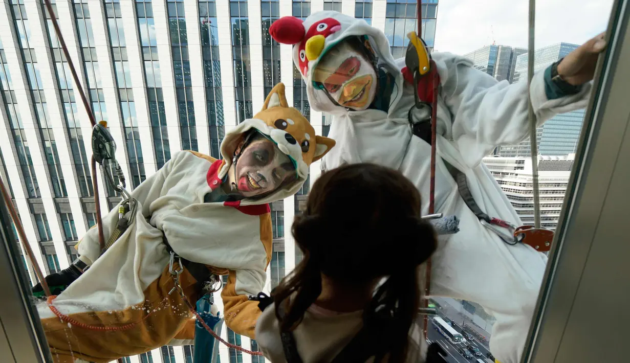Seorang anak melihat pembersih jendela wanita berkostum ayam jago dan anjing di kawasan perbelanjaan dan bisnis Tokyo, Jepang (20/12). Ayam jago merupakan binatang zodiak tahun ini dan anjing untuk tahun depan. (AP Photo / Shizuo Kambayashi)