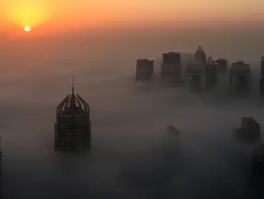 Pemandangan saat matahari terbit memancarkan sinar yang berwarna oranye keemasan diantara gedung pencakar langit di Kota Dubai, Uni Emirat Arab, Senin (5/12). Telihat banyak dari puncak gedung-gedung itu menembus awan. (AFP/Rene Slama)