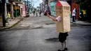 Pensiunan perawat, Feridia Rojas memakai kotak kardus berbentuk rumah untuk melindungi dirinya dari penyebaran Covid-19 di Havana, Kuba, 8 Juli 2020. Kardus pelindung pensiunan berusia 82 tahun itu dilengkapi pesan yang ditulis tangan dalam bahasa Spanyol "I'm home, and you?." (AP/Ramon Espinosa)
