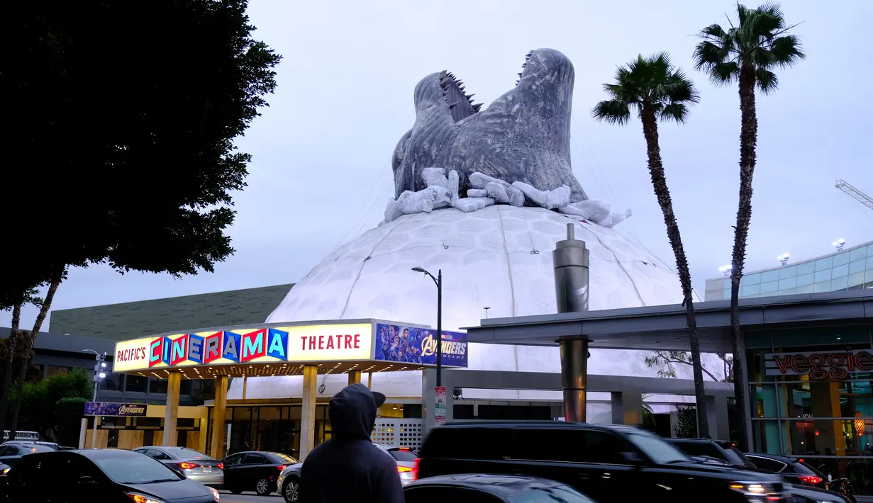 Kendaraan melintasi bioskop Cinerama Dome yang atapnya dihiasi godzilla raksasa di Hollywood, California, AS pada 20 Mei 2019. Hinggapnya godzilla raksasa untuk menyambut sekuel Godzilla: King of the Monsters yang akan dirilis pada 31 Mei 2019. (Photo by Chris Delmas / AFP)