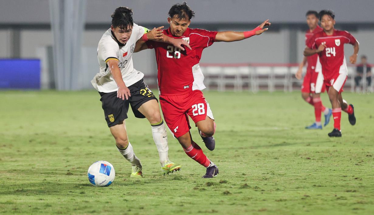 Pemain Timnas Indonesia U-17, I Komang Semadi berduel dengan pemain China U-17, Li Junpeng dalam pertandingan uji coba internasional di Indomilk Arena, Tangerang, pada Rabu (11/2/2026) malam WIB. (Bola.com/Abdul Aziz)