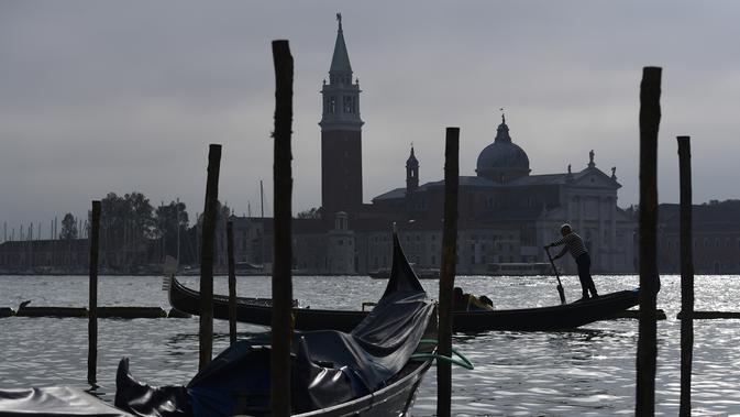 Gondola mengangkut wisatawan yang dekat dengan perairan Riva degli Schiavoni dengan latar gereja San Giorgio Maggiore di Venice (4/11/2019). Di kawasan ini ada pejalan kaki yang ramai meskipun sering penuh sesak di sepanjang tepi pantai, yang terletak di Cekungan St. Mark. (AFP Photo/Miguel Medina)