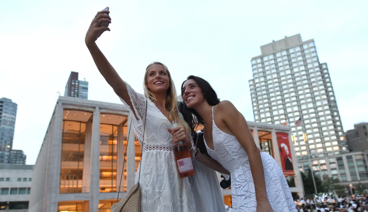 Dua orang wanita berswafoto saat menghadiri Diner en blanc (Dinner in White) di alun-alun Lincoln Center, New York, Selasa (22/8). Acara yang dimulai sejak 2011 di New York ini dirilis pertama kali di Prancis, sekitar 30 tahun silam (TIMOTHY A. CLARY/AFP)