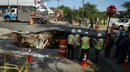 Sejumlah petugas saat menyelidiki sebuah lubang besar (sinkhole) di wilayah Brooklyn, New York, Selasa (4/8/2015). Lubang yang terbentuk di persimpangan pemukiman Sunset Park itu disebabkan erosi dan merusak pipa air serta aspal jalan. (AFP/Kena Betancur)
