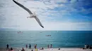 Seekor burung camar terbang di atas para pengunjung pantai di Etretat, Prancis barat laut (17/7). Kota ini merupakan kota wisata dan pertanian yang terletak sejauh 32 km (20 mi) dari Le Havre. (AFP Photo/Charly Triballeau)