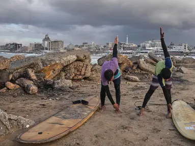Warga Palestina, Khalil Abu Jayyab (kanan) dan Tahseen Abu Assi melakukan pemanasan sebelum berselancar di pantai Kota Gaza, Minggu, 28 Desember 2025. Pasca diberlakukannya gencatan senjata fase pertama yang didukung oleh Amerika Serikat mulai berlaku pada 10 Oktober 2025, warga Palestina mulai kembali ke Kota Gaza. (AP Photo/Jehad Alshrafi)