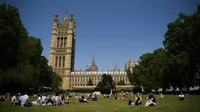 Orang-orang berbincang saat bersantai di bawah sinar matahari di Victoria Tower Gardens dekat Gedung Parlemen di London (23/7/2019). Suhu melonjak di atas 30C (86F) di Inggris pada 23 Juli dengan para peramal cuaca memperkirakan suhu setinggi 37C (96.8F) sebelum akhir pekan. (AFP Photo/Ben Stansall)