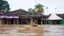 Seorang anak laki-laki menggunakan kotak untuk mengarungi banjir setelah banjir di Serang, Provinsi Banten (1/3/2022).  Berdasarkan data sementara dari Polres Serang Kota, ada 20 titik banjir yang merendam pemukiman warga di Kota Serang. (AFP/Dziki Oktomauliyadi)
