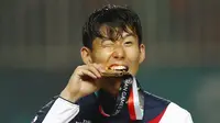 Penyerang Korea Selatan, Son Heung-min, menggigit mendali, usai menjuarai Asian Games dengan mengalahkan Jepang di Stadion Pakansari, Jawa Barat, Sabtu (1/9/2018). (AP/Bernat Armangue)