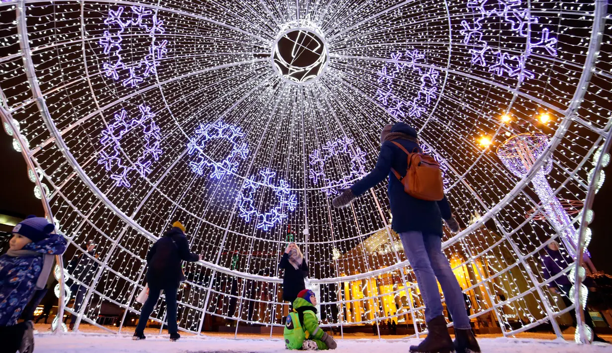 Pengunjung berjalan di dalam bola natal raksasa yang dipajang di Octyabrskaya Square dan dekorasi untuk menyambut perayaan Natal 2018 dan Tahun Baru 2019 di Minsk, Belarus, Selasa (18/12). (AP Photo/Sergei Grits)