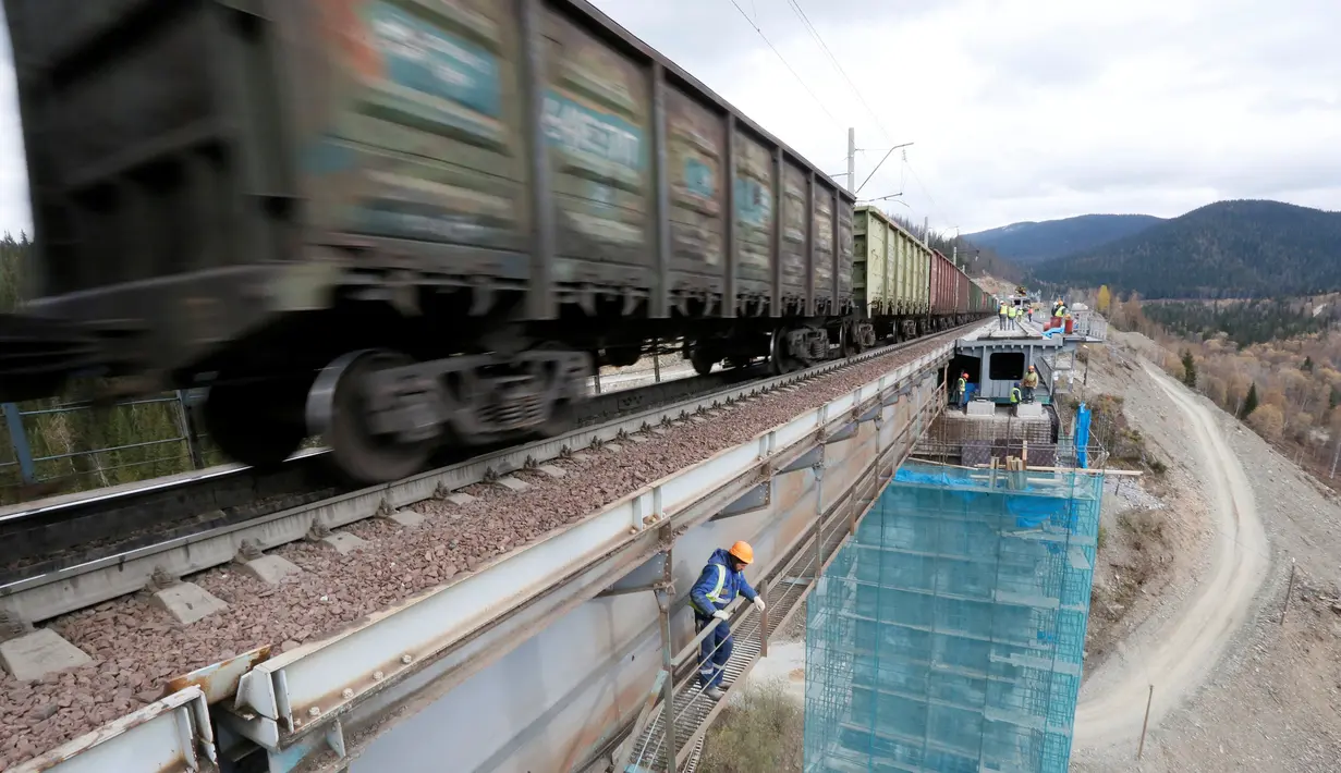 Kereta barang melintas saat pekerja menyelesaikan proyek jembatan kereta api tertinggi di Rusia, yang berada di Taiga, daerah timur Pegunungan Sayan Ridge dekat stasiun kereta Dzheb di Krasnoyarsk, Rusia (10/11). (REUTERS/Ilya Naymushin)