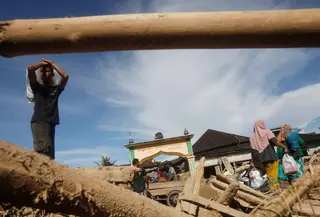 Selain rumah warga terdampak, kayu-kayu gelondongan juga masih terlihat tertumpuk di sepanjang aliran Sungai Aek Garoga dan Sungai Batang Toru. Tampak dalam foto, para penyintas berjalan melewati tumpukan kayu yang tersapu banjir bandang di Batang Toru, Sumatra Utara, Selasa 2 Desember 2025. (AP Photo/Binsar Bakkara)