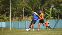 Yann Motta (rompi biru) dibayangi Dalberto Luan dalam sesi latihan Arema FC di lapangan ARG, Kabupaten Malang, Rabu (02/07/2025). (Iwan Setiawan/Bola.com)