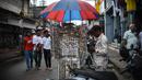 Seorang pedagang kaki lima menggunakan payung untuk melindungi anting-antingnya dari hujan di Kochi, negara bagian Kerala, India, Rabu (6/7/2022). Negara bagian selatan itu telah mewajibkan penggunaan masker di tempat-tempat umum menyusul meningkatnya kasus COVID-19. (AP Photo/ RS Iyer)