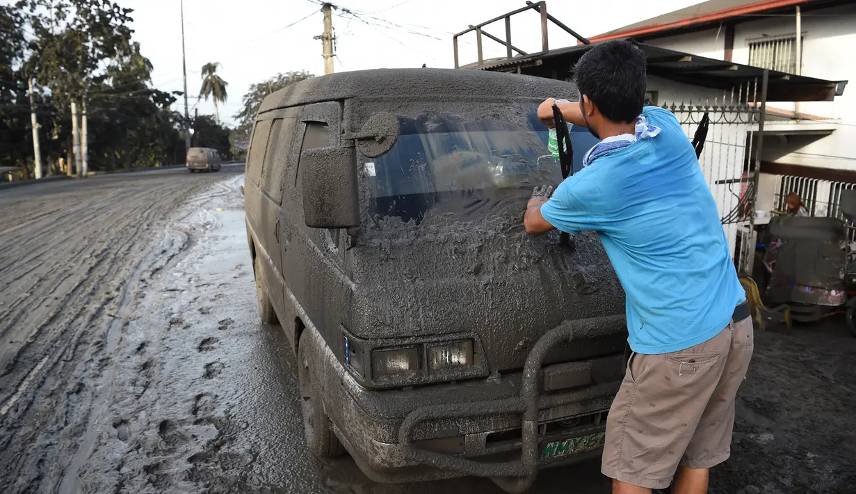 Warga membersihkan abu vulkanik dari kendaraan mereka setelah erupsi Gunung Taal di Tagaytay, Provinsi Cavite, Filipina, Senin (13/1/2020). Gunung yang terakhir meletus pada tahun 1977 tersebut melontarkan abu vulkanik mencapai 50.000 kaki (15.000 meter) ke atmosfer. (TED ALJIBE/AFP)